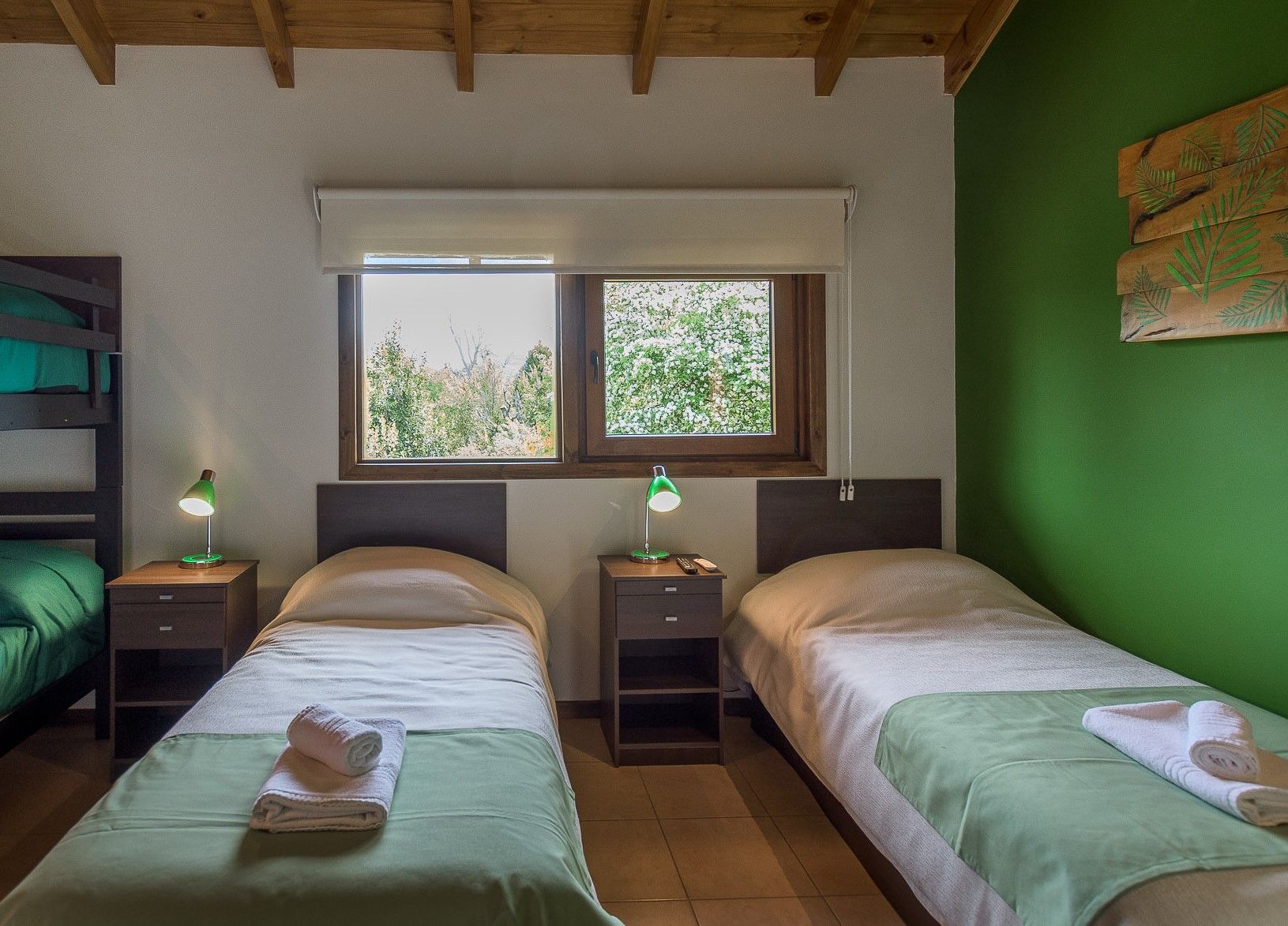 Un dormitorio con una litera, dos camas individuales con mantas verdes, ropa de cama blanca, mesitas de noche, lámparas y una pared verde.