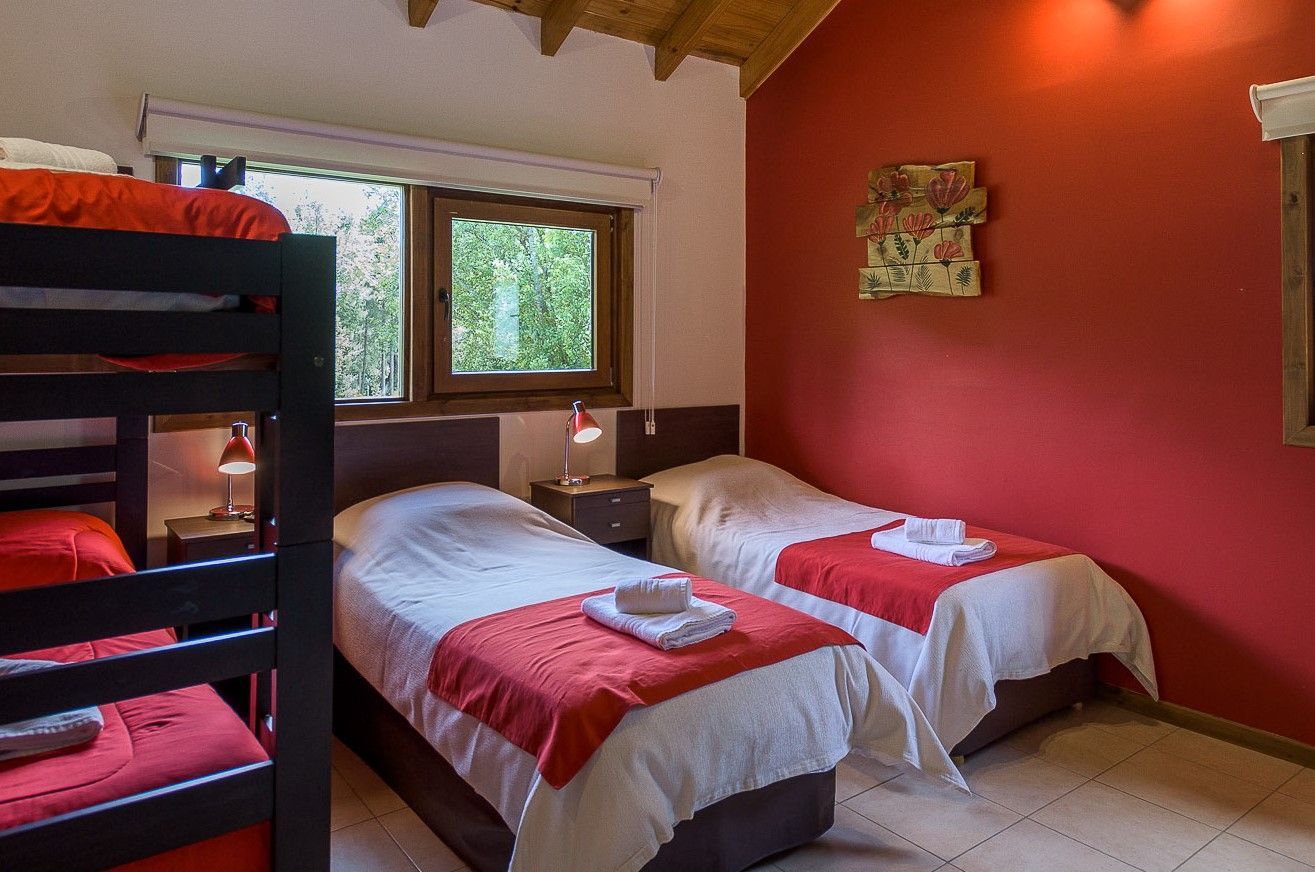 Una habitación de hotel con una litera negra, dos camas individuales con sábanas blancas y caminos de mesa rojos, y una pared decorativa roja.
