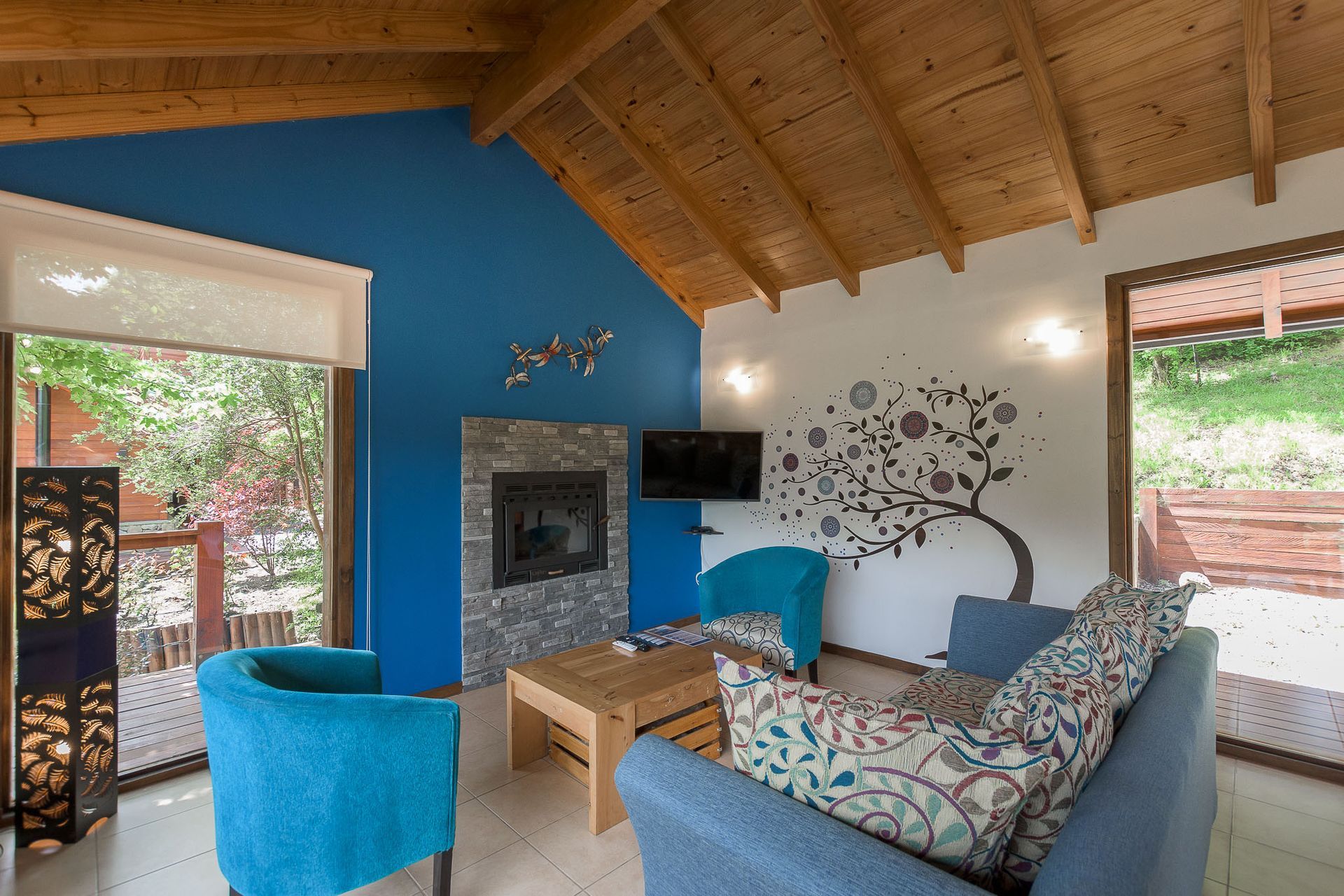 Sala de estar con una pared decorativa azul, chimenea de piedra, techo abovedado de madera, un sofá azul y un sillón a juego.