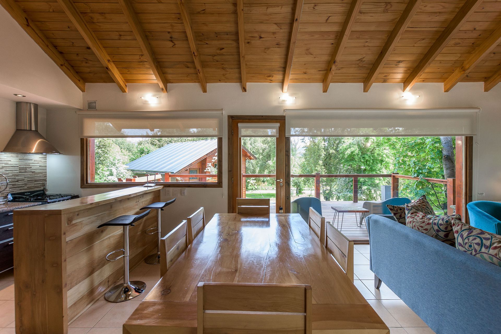 Un espacio moderno de concepto abierto con mesa de comedor de madera, barra de desayuno y vistas a frondosos árboles a través de grandes ventanales.
