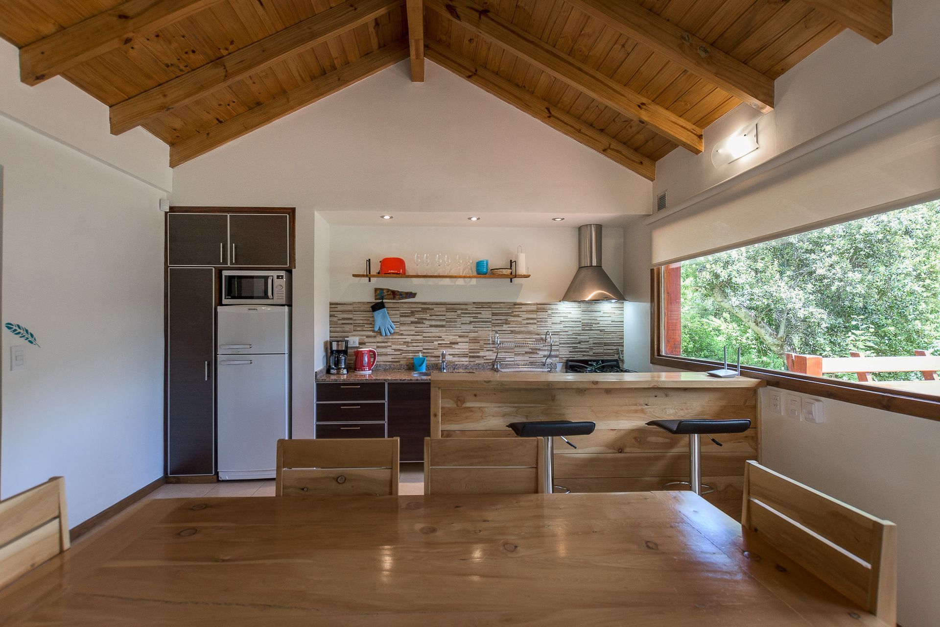 Una cocina de estilo rústico con mesa de comedor de madera, barra de desayuno, electrodomésticos de acero inoxidable y techos abovedados de madera.