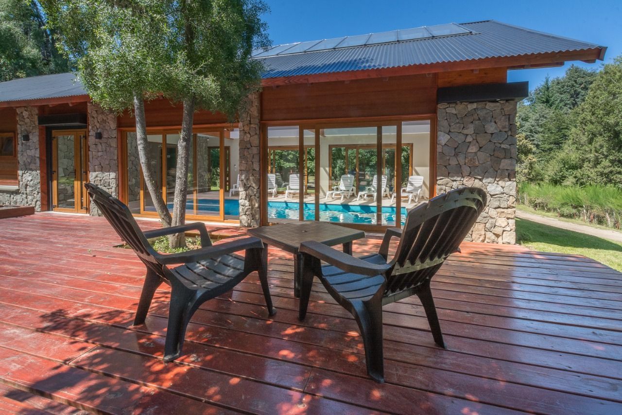 Dos sillas negras en una terraza de madera con vistas a una piscina, junto a una cabaña rústica con detalles de piedra.