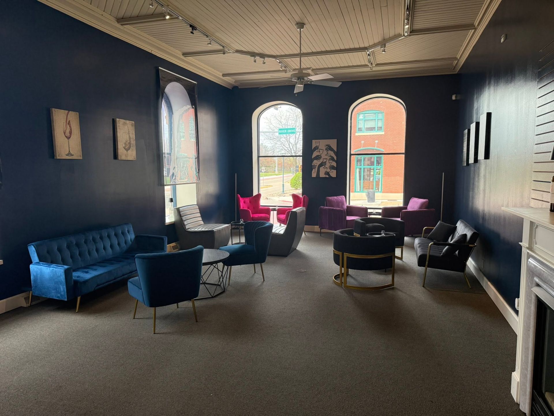 Stylish lounge with blue chairs, pink pillows, arched windows, and a large black wall in soft daylight