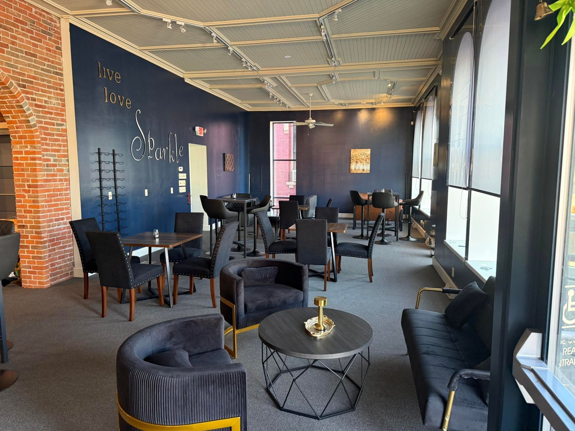 Modern lounge with dark walls, black chairs, round tables, and large arched windows