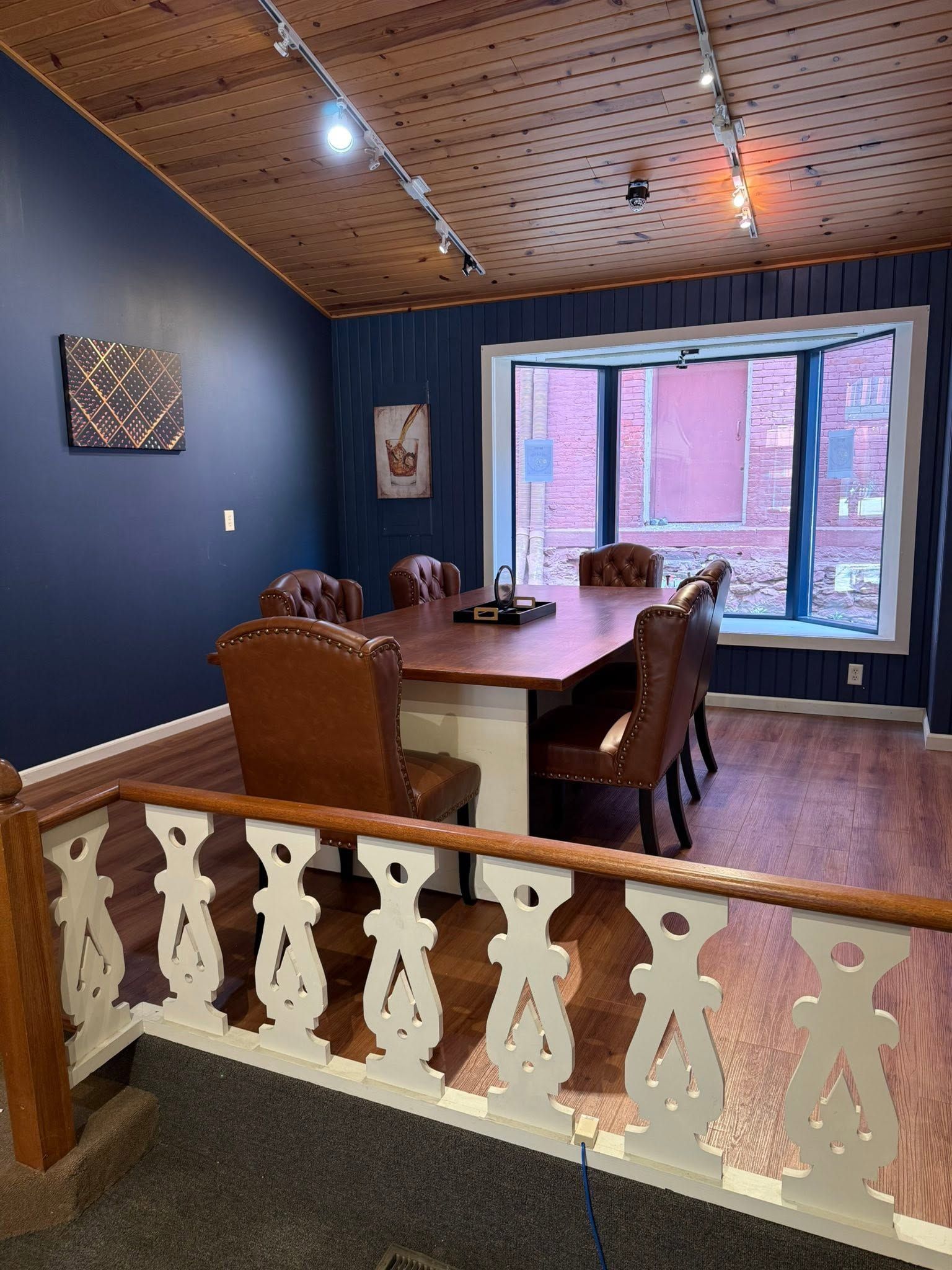 Dining room with blue walls, wood table, patterned ceiling, and large window seat overlooking brick outside