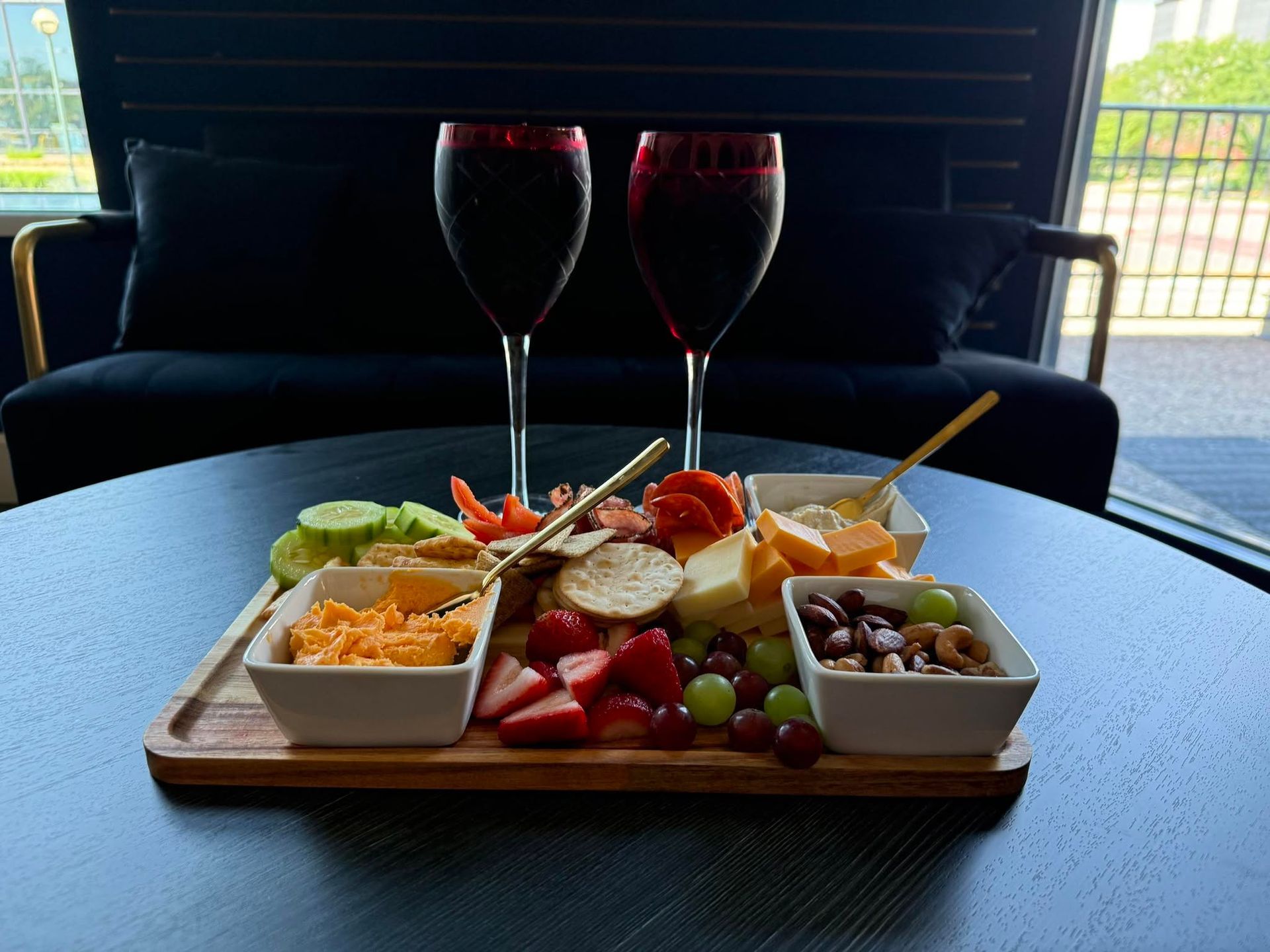 Charcuterie board with fruit, nuts, cheese, and bread on a table with two glasses of red wine outdoors