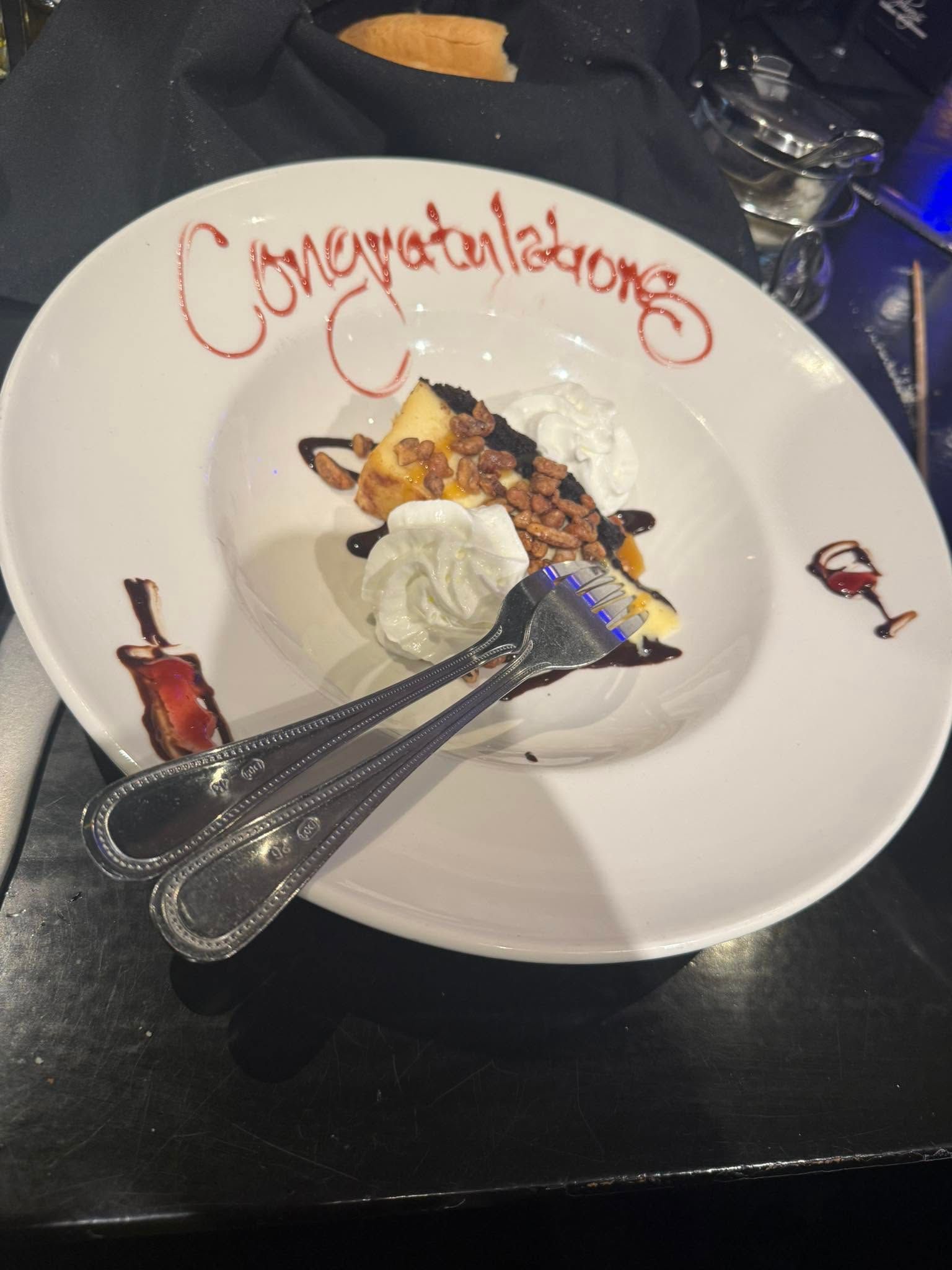 Dessert plate with “Congratulations” in red icing and a scoop of ice cream on a dark table.
