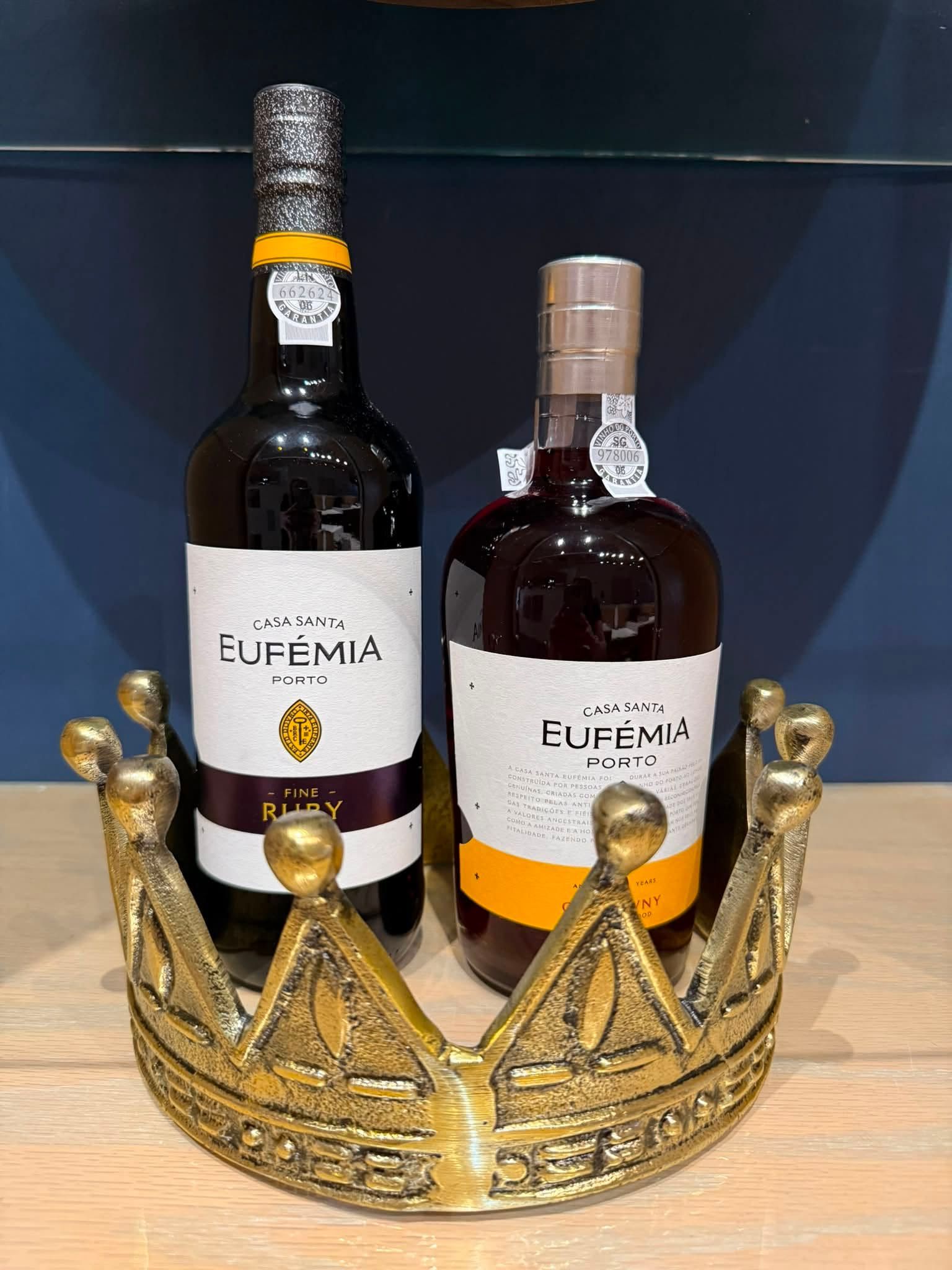 Two Fubemá bottles in a gold crown display, one dark wine and one clear amber spirit.
