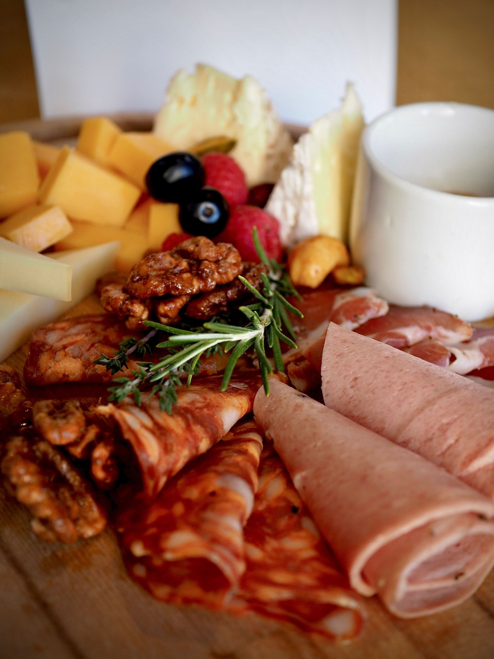 Charcuterie board with cheeses, sliced meats, olives, crackers, and a white dip cup