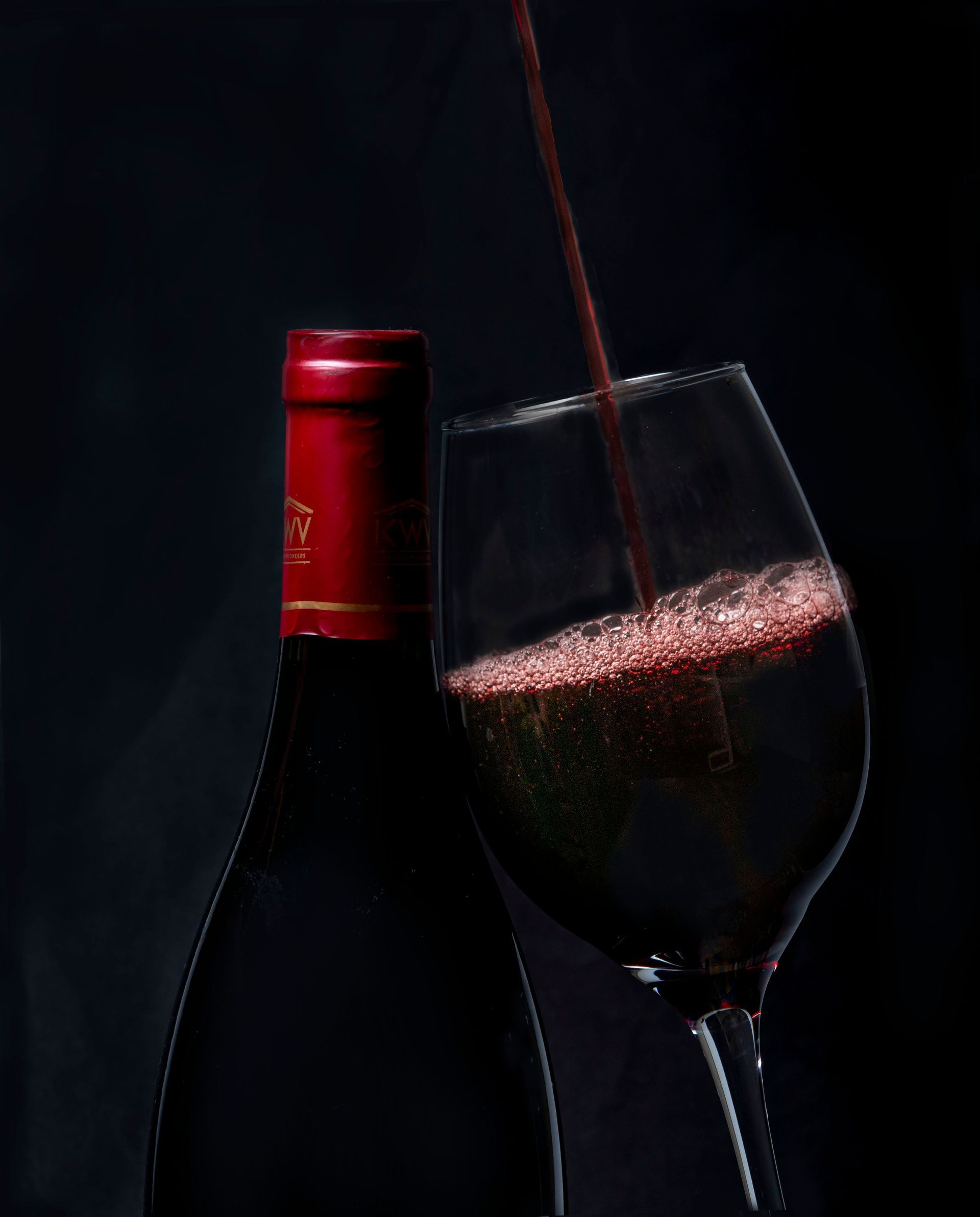 Red wine being poured into a tilted glass beside a bottle on a dark background