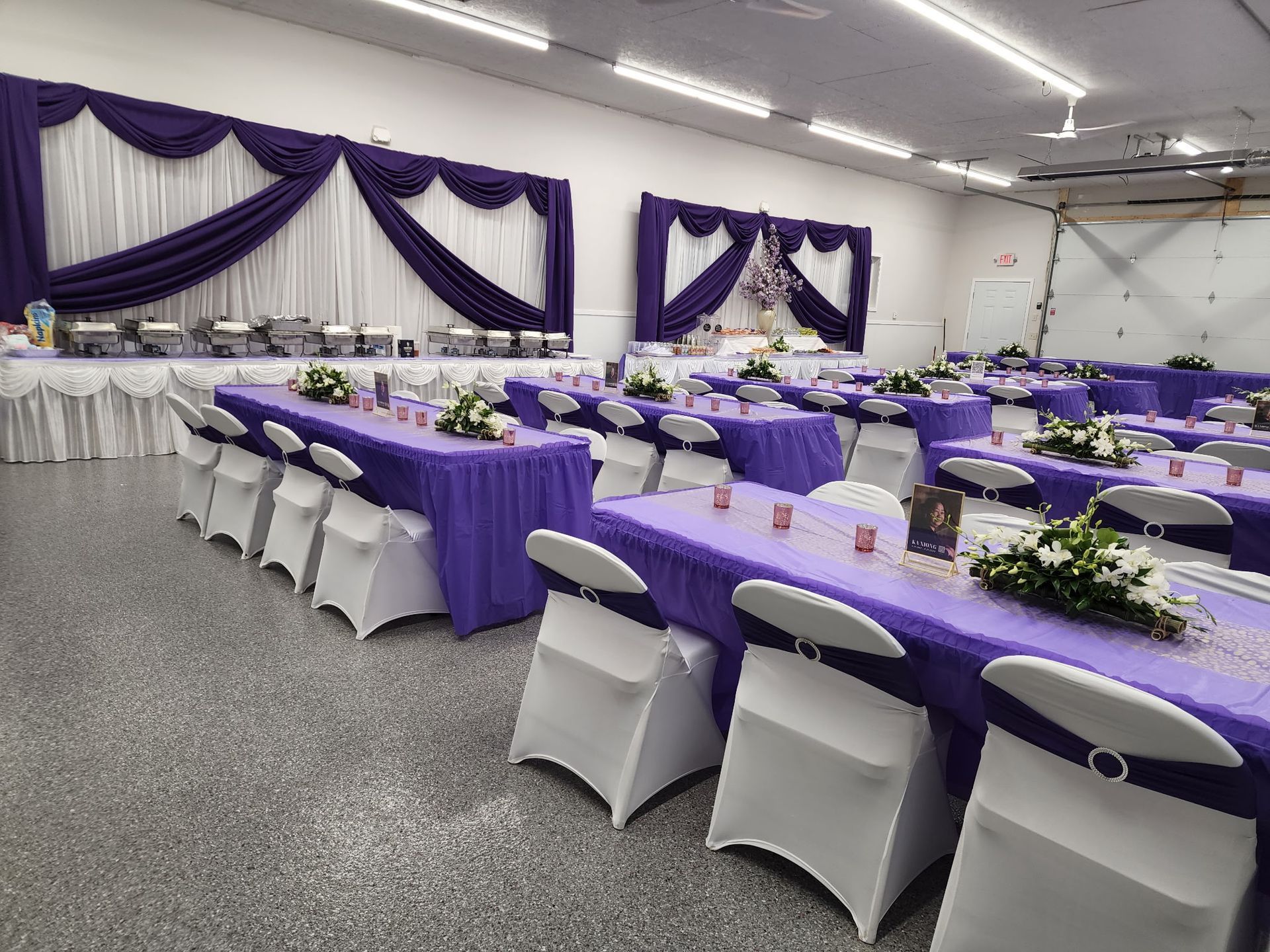 Purple and white banquet hall set with round tables and chair covers for an event