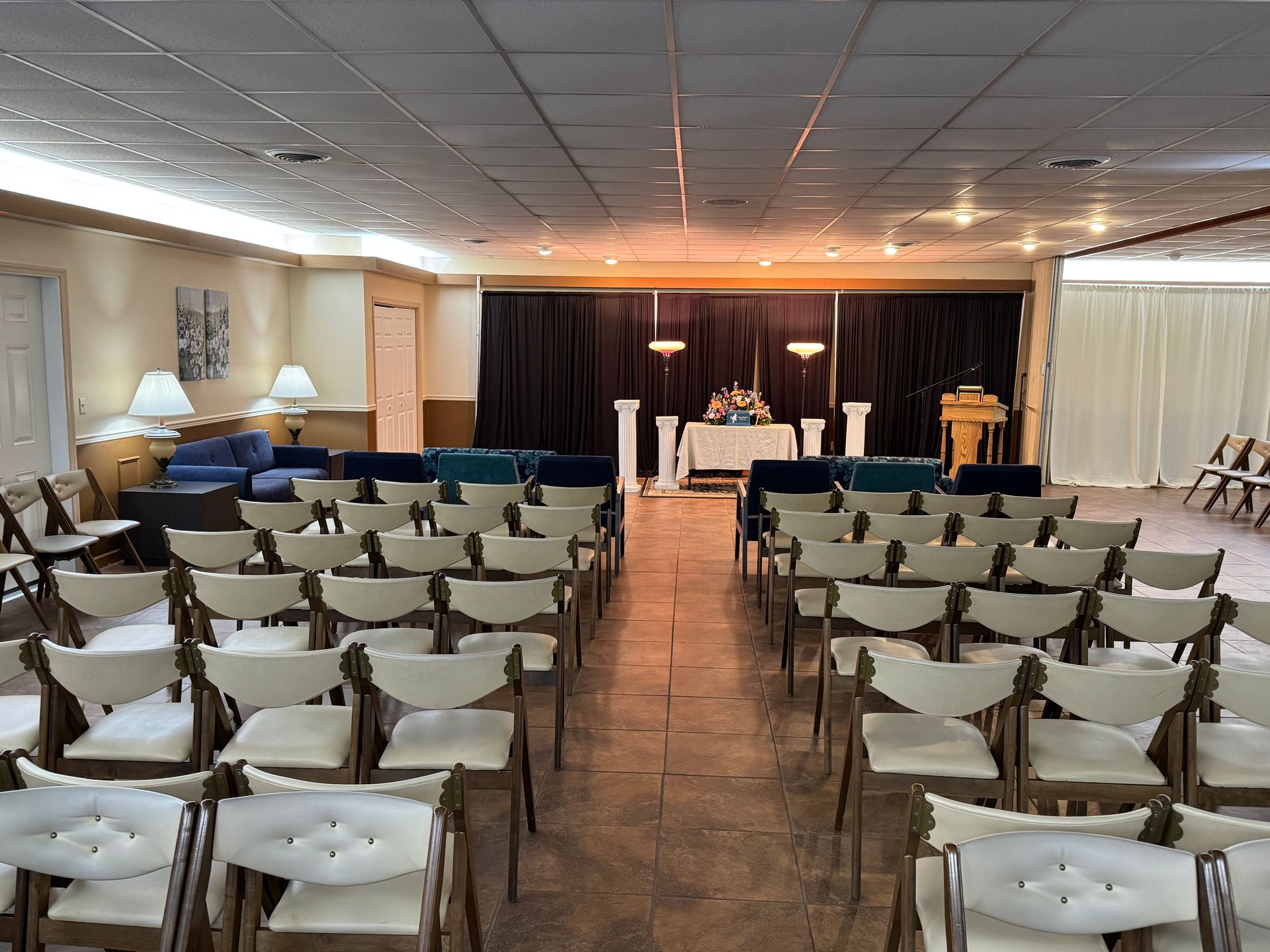 Rows of white chairs facing a small stage in a banquet hall with dark curtains and warm lighting