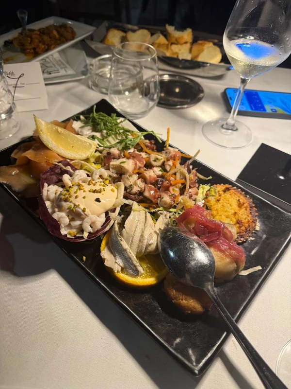 Un piatto rettangolare con vari antipasti di pesce, tra cui pesce marinato, polpo e crostacei, su un tavolo di ristorante.