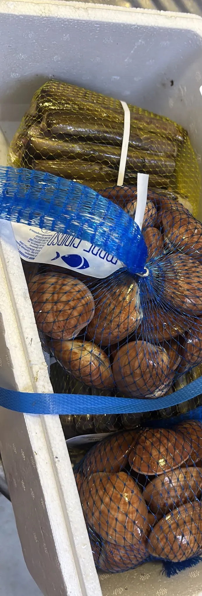 Un contenitore di polistirolo contiene un fascio di foglie di vite arrotolate di colore verde scuro e diverse retine di molluschi marroni.