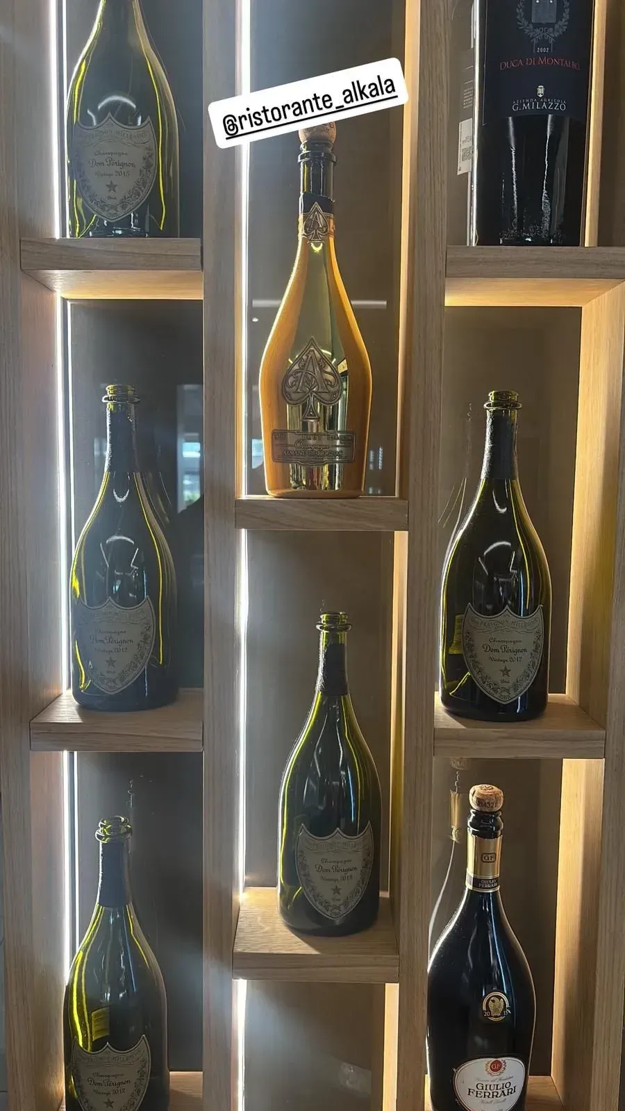 Una mensola in legno che espone sette bottiglie di champagne, tra cui diverse bottiglie di Dom Pérignon e una bottiglia dorata.
