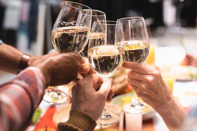 Diverse persone, attorno a un tavolo da pranzo, alzano insieme i calici di vino bianco per un brindisi.
