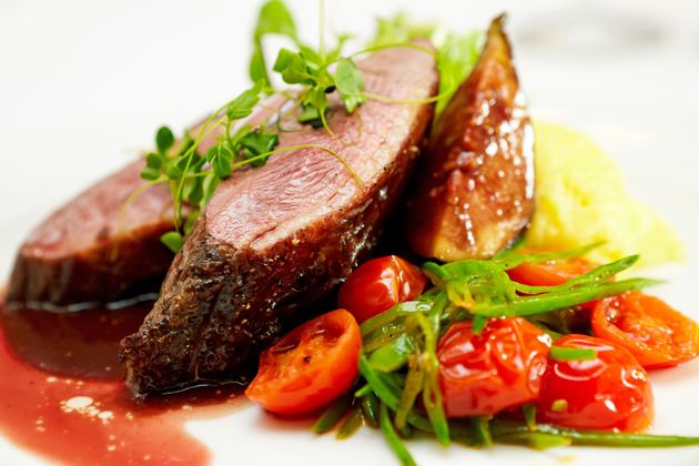 Un piatto unico composto da anatra arrosto a fette, mezzo fico, purè di patate, fagiolini saltati e pomodorini.