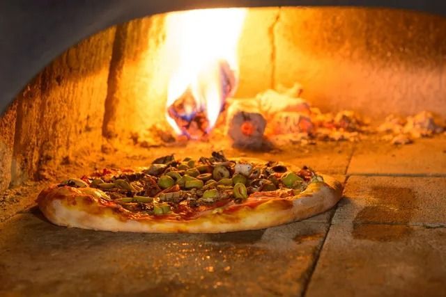 Una pizza condita con olive che cuoce in un forno a legna, con le fiamme visibili sullo sfondo.
