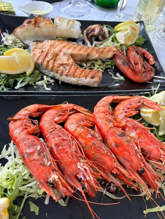 Due piatti neri di frutti di mare grigliati, con un filetto di salmone, gamberi e spicchi di limone serviti su un letto di lattuga tritata.