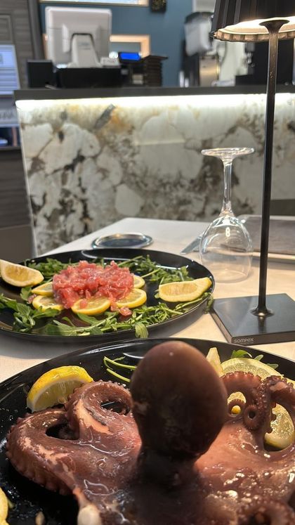 Due piatti di frutti di mare gourmet, con un polpo intero alla griglia e una tartare di tonno, serviti in un ristorante moderno.