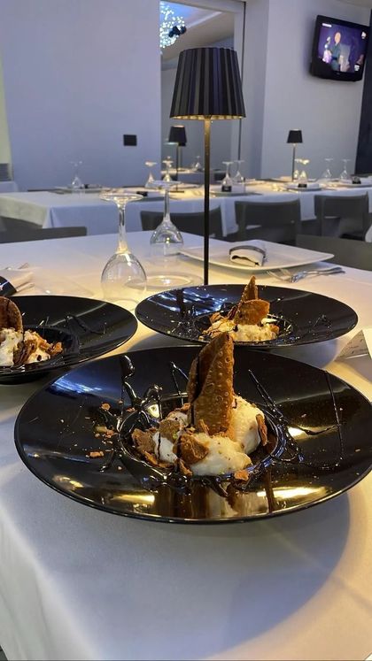 In un ristorante illuminato da una lampada moderna, tre dessert serviti su piatti neri su un tavolo bianco.