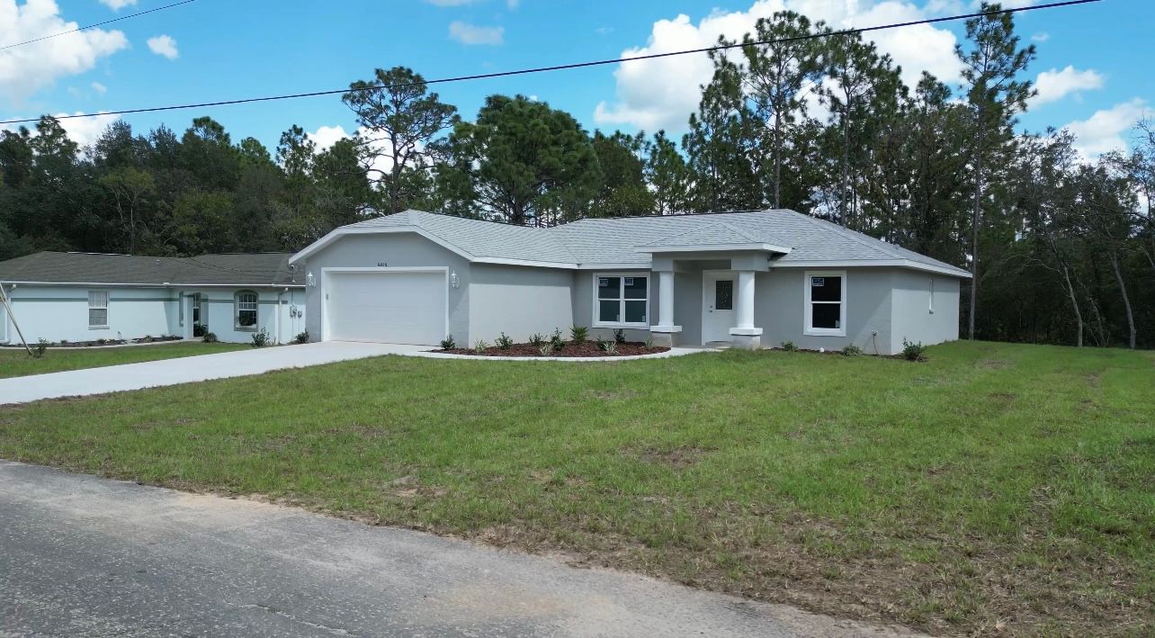 A light gray house with a garage, driveway, and front yard.