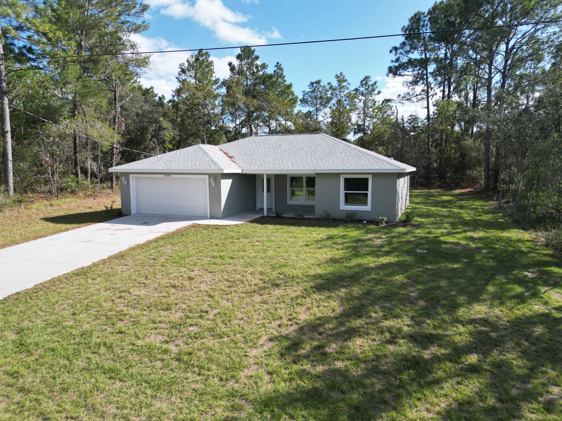 Gray house with a two-car garage, on a grassy lot, surrounded by trees.
