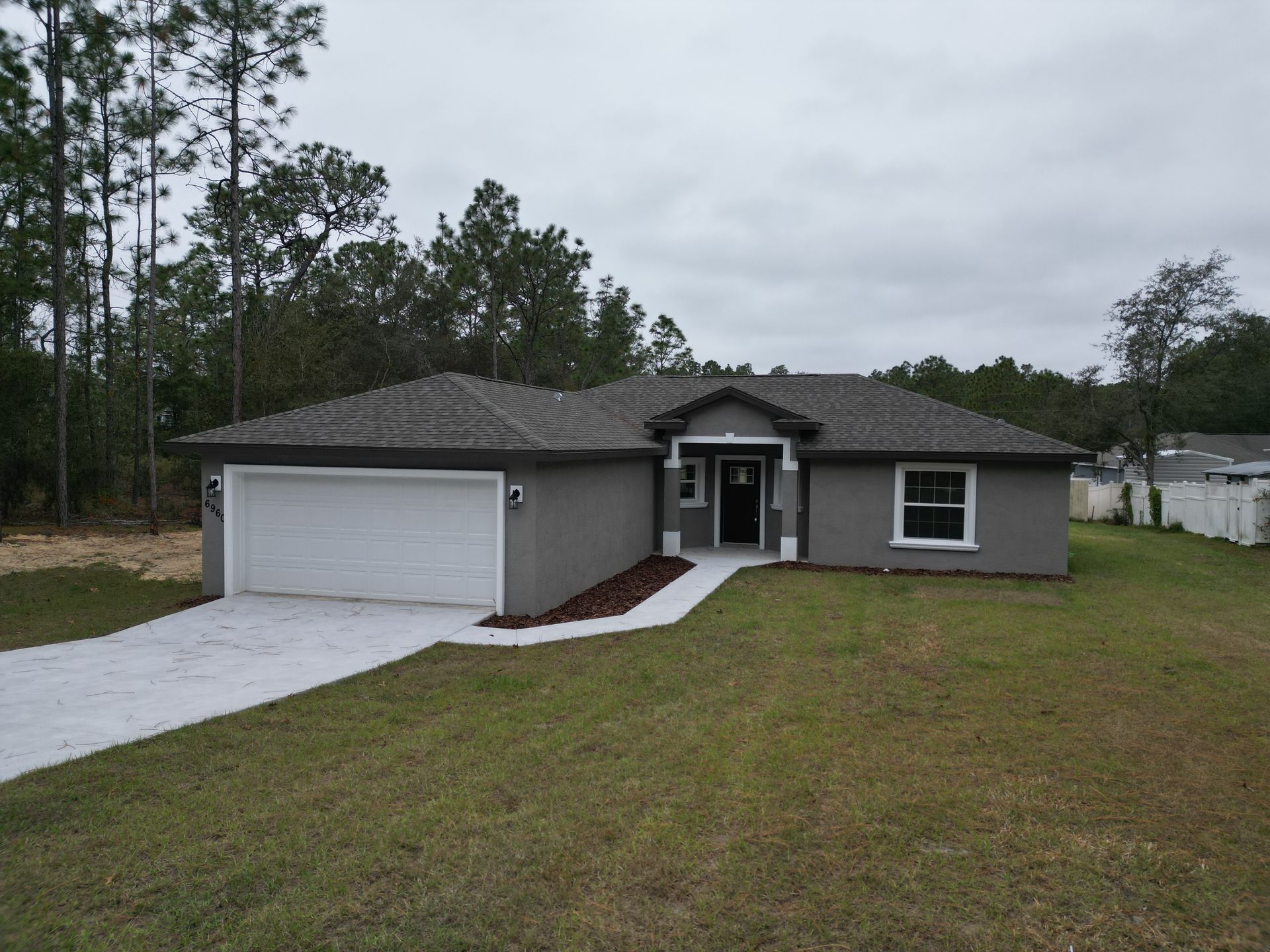 Gray stucco house with white garage door and trim, concrete driveway, and grassy yard.