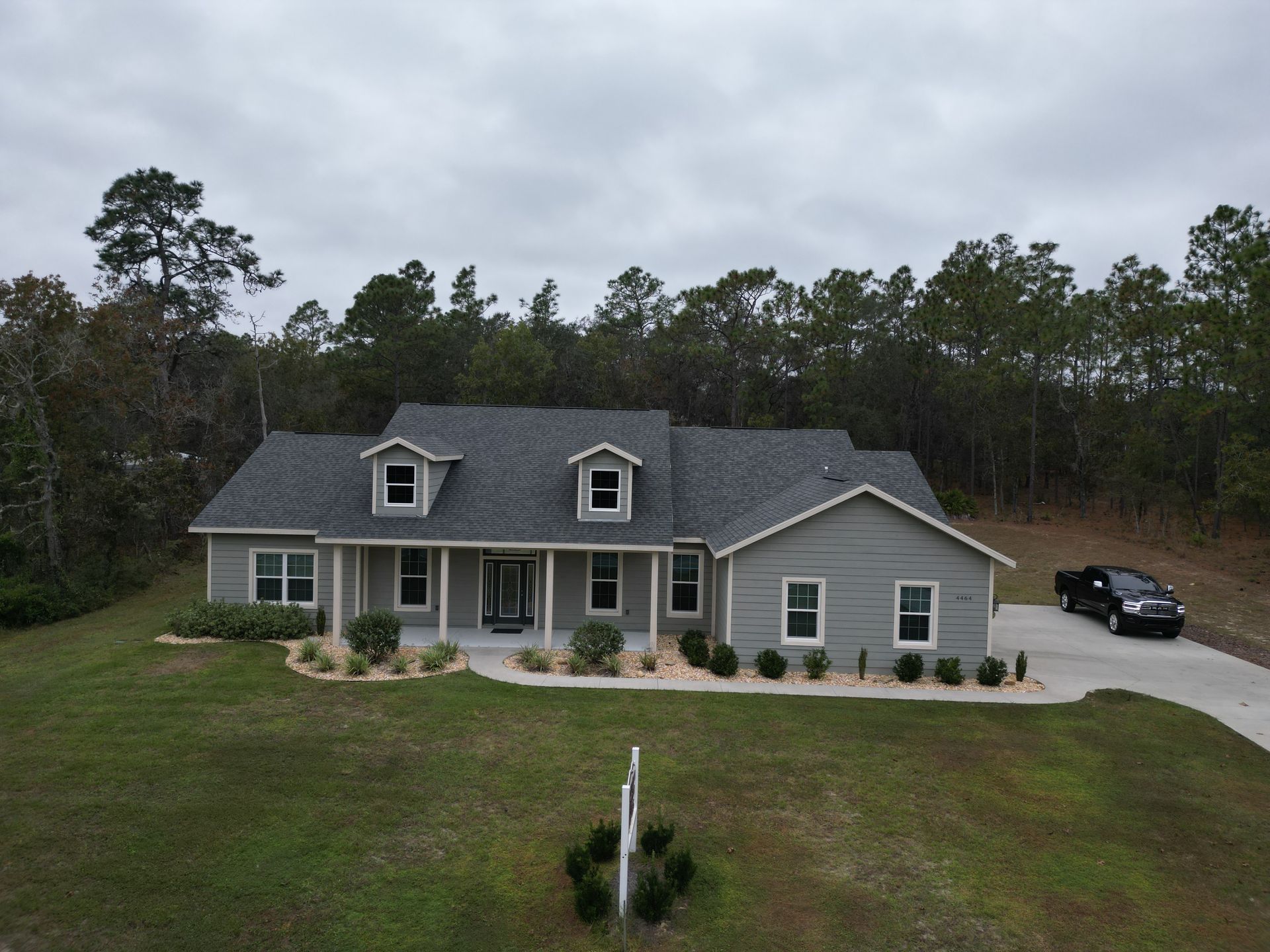 Gray house with dark gray roof, three dormers, and a car parked in the driveway. Trees in the background.