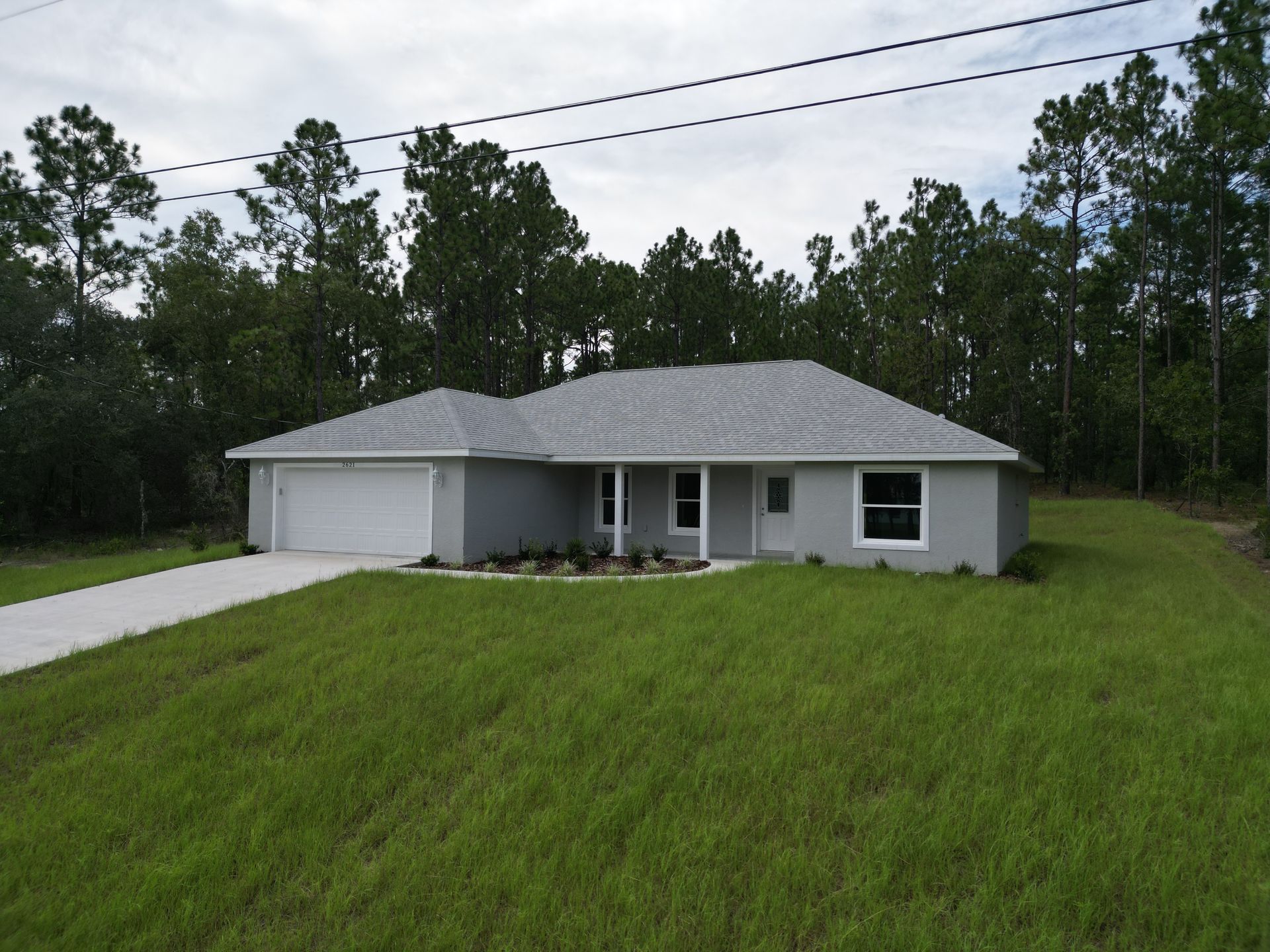 Gray house with a two-car garage, white trim, and a green lawn. Trees in the background.