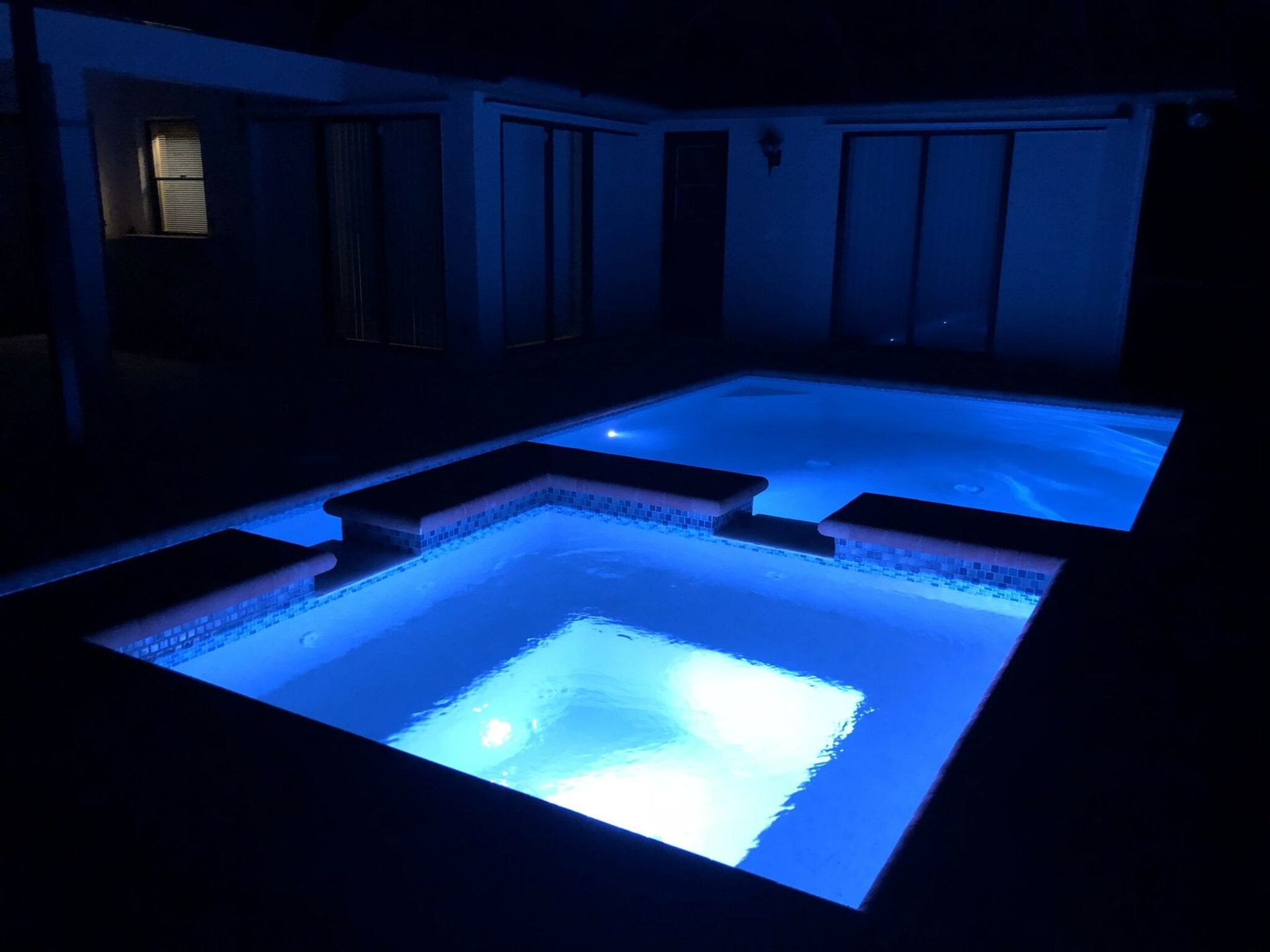 A swimming pool is lit up at night with blue lights built by Into h2o Pools & Spas Cape Coral