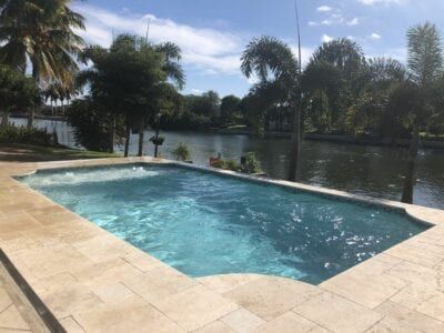 A large swimming pool surrounded by palm trees next to a body of water.