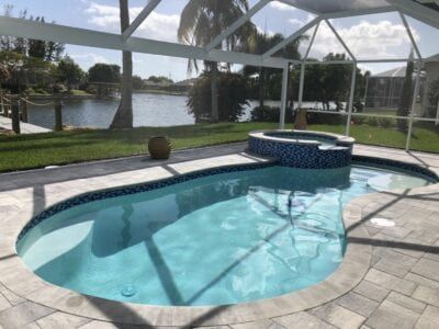 A large swimming pool is surrounded by a screened in area.
