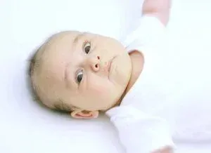 Baby lying on a white surface, looking up with a soft expression.