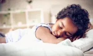 Young child sleeping on a bed, resting head on pillow.