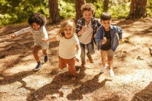 Four children running in a sunny forest clearing; shadows on the ground.