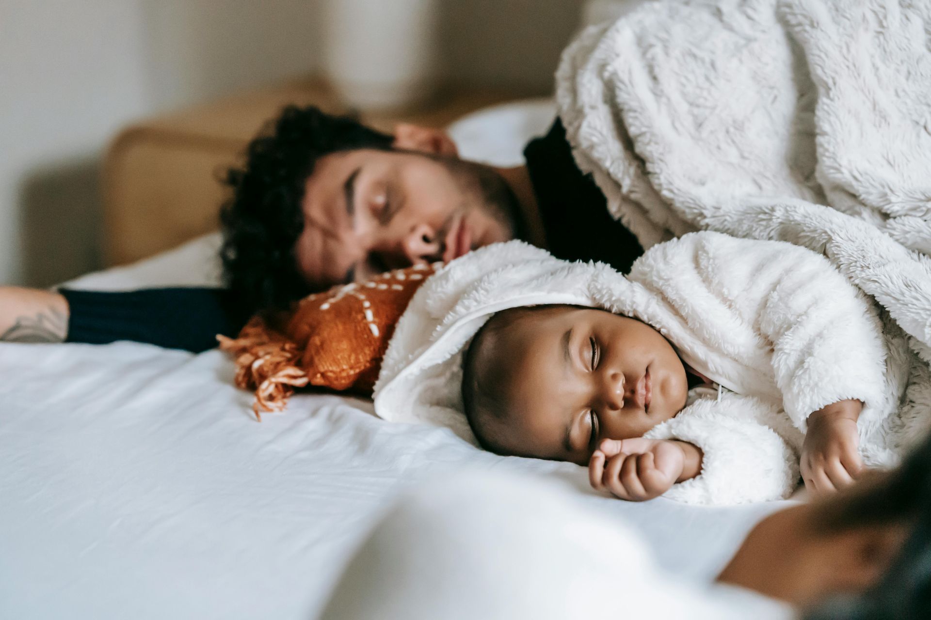 Man and baby sleeping on a white bed under a blanket.
