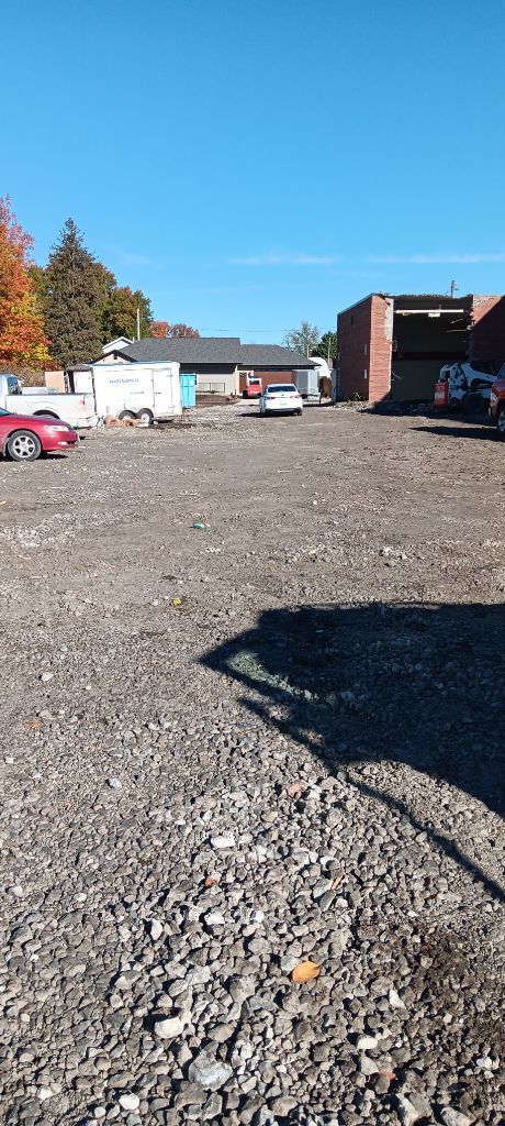 Gravel parking lot with parked vehicles, brick buildings, and a clear blue sky on a sunny day
