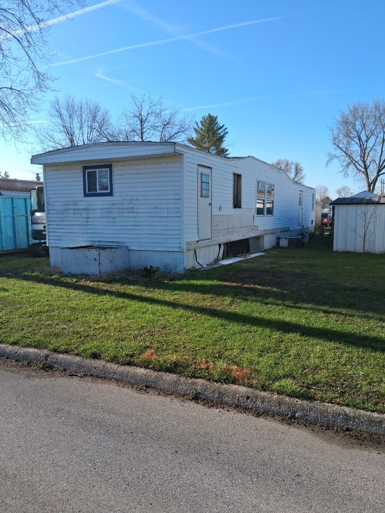 White mobile home with blue trim in a grassy lot under a clear sky