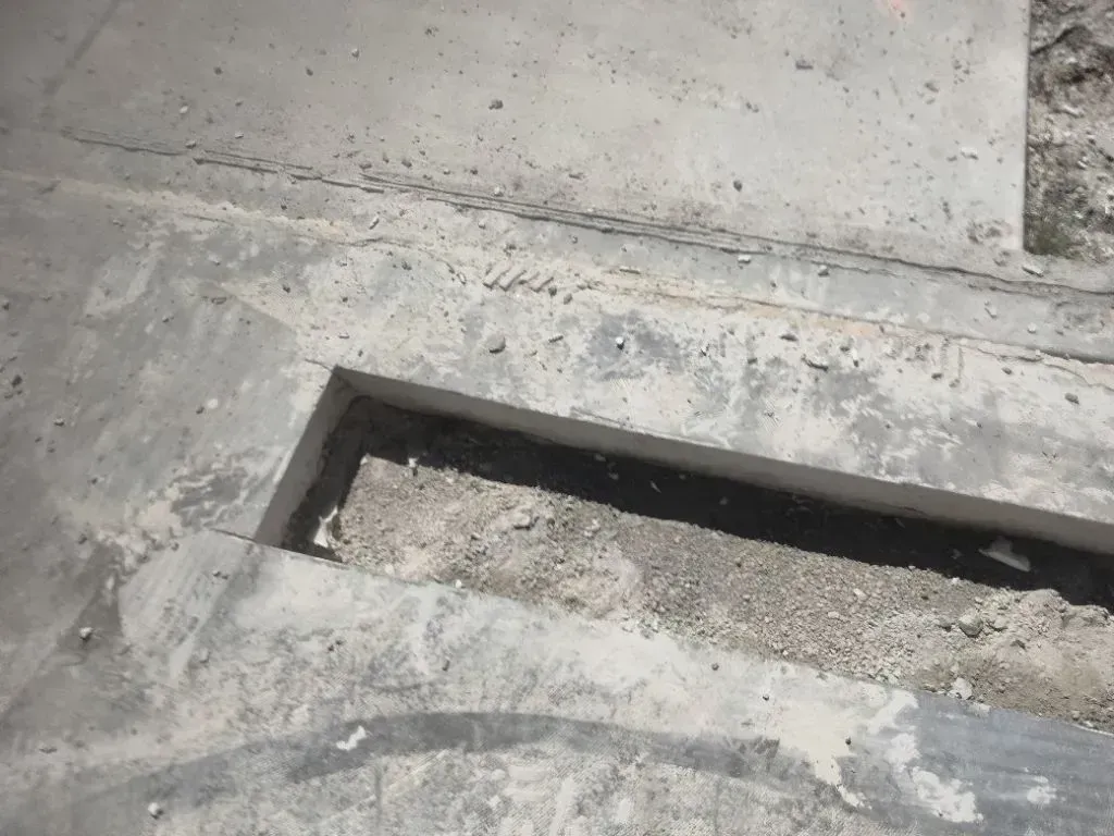 A rectangular section of a concrete sidewalk has been cut out, exposing the gravel and dirt ground beneath.