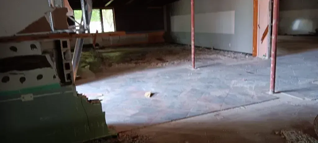 A dimly lit, unfinished indoor construction site with concrete flooring, support pillars, and exposed wall materials.