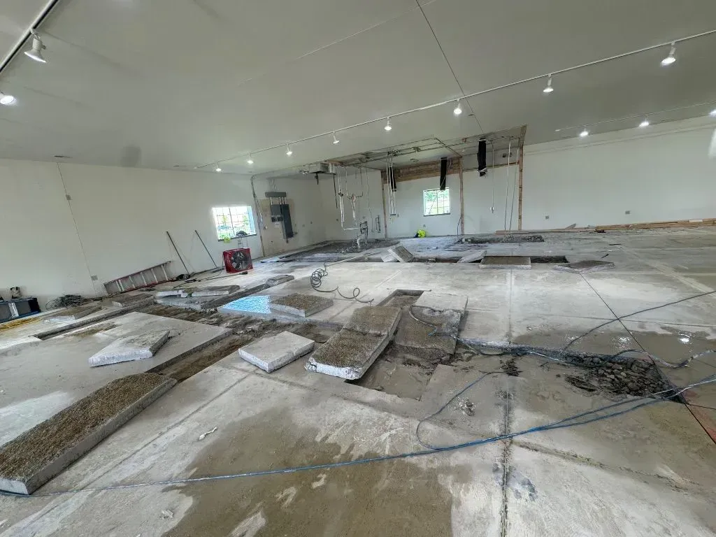 Interior view of a construction site with a partially demolished concrete floor and exposed dirt trenches.
