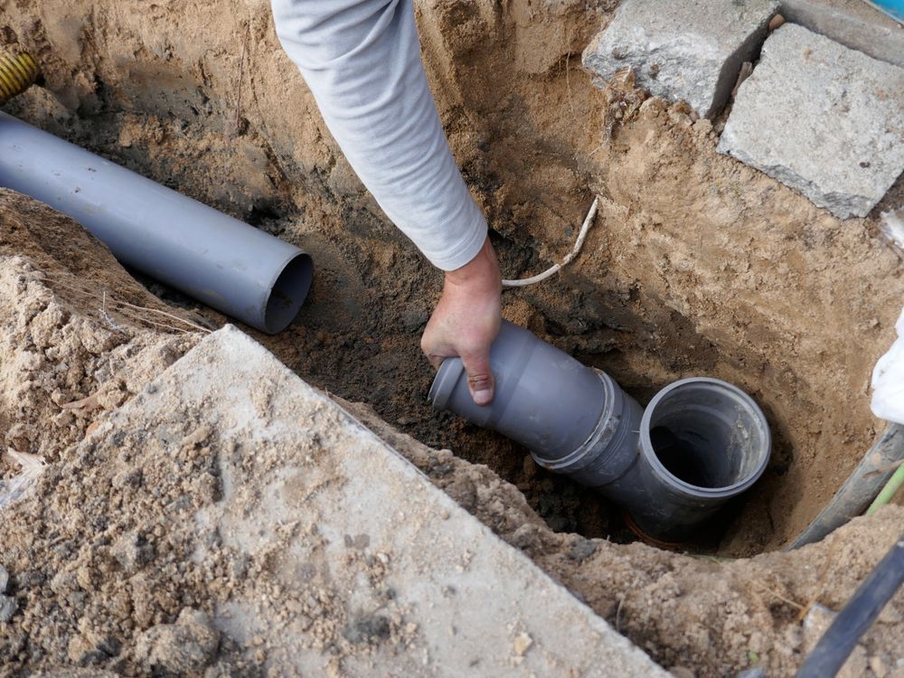 Worker Connecting Gray Pvc Pipes in An Excavated Trench Outdoors — Bridge Plumbing & Trades in Nowra, NSW