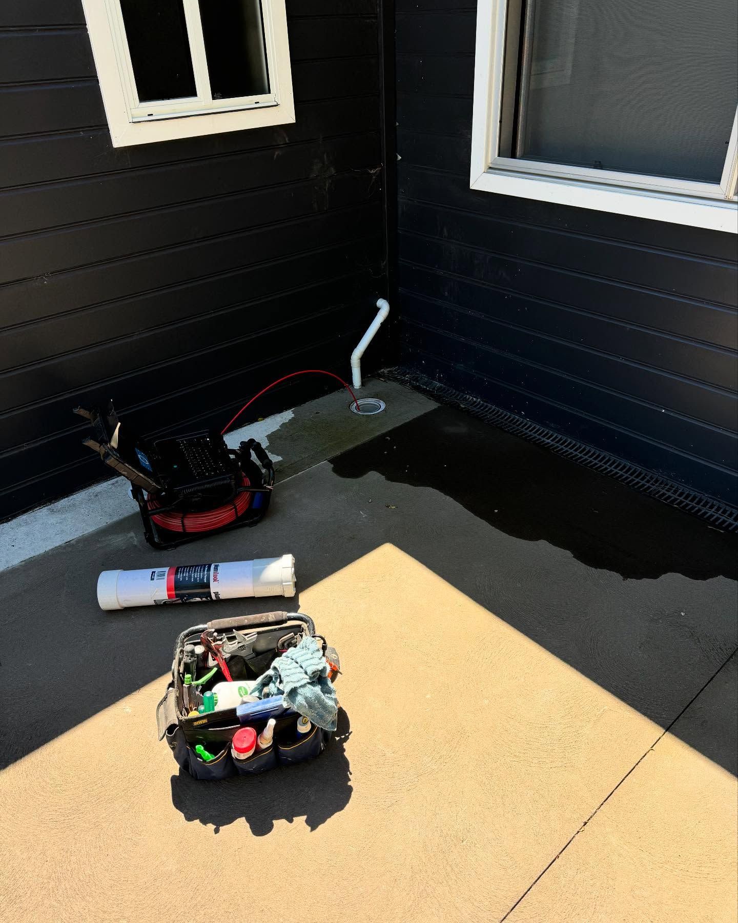 Water Pooling Around a White Pipe Near a Dark Building Corner — Bridge Plumbing & Trades In Kiama, NSW