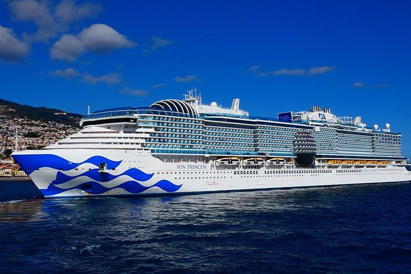 Large white cruise ship with blue wave graphics sailing on dark blue water under a clear sky