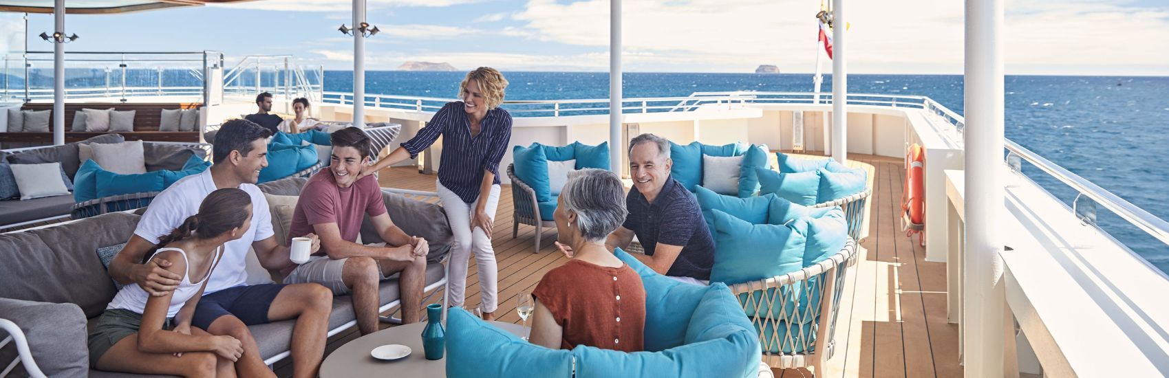 People relaxing on a boat deck with blue cushions, a yacht railing, and open ocean in the background