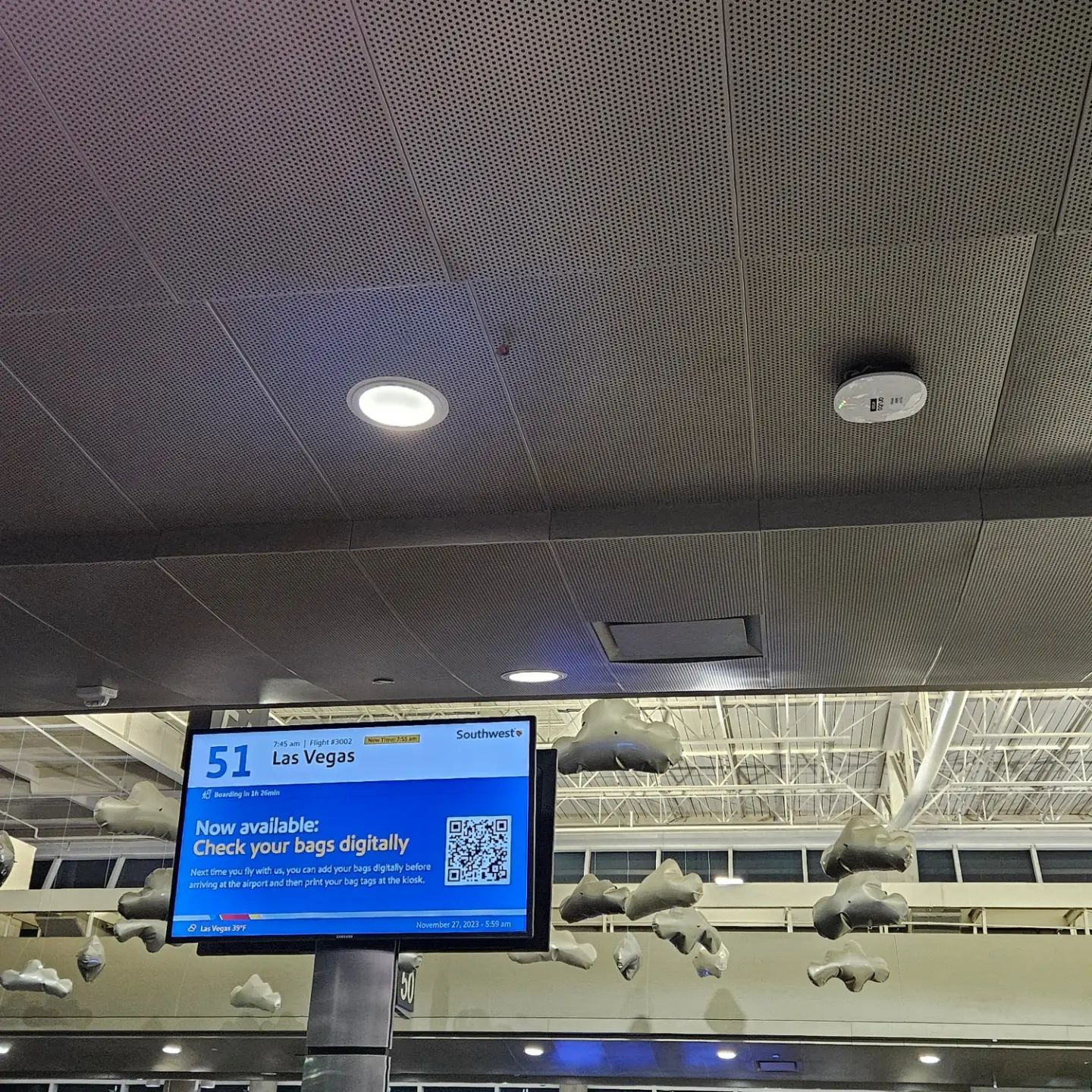 Airport gate monitor showing flight information in a terminal ceiling area