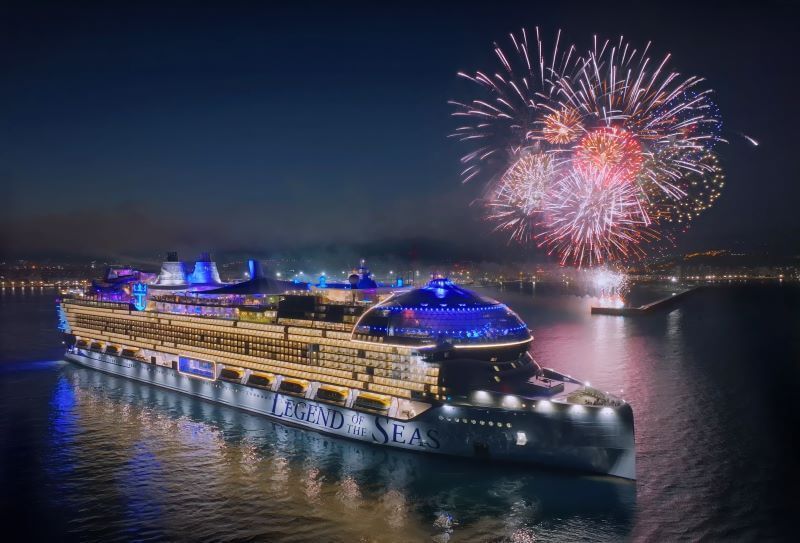Cruise ship at night on calm water with fireworks bursting overhead