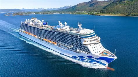 Large white cruise ship sailing on blue water near a green coastline and mountains