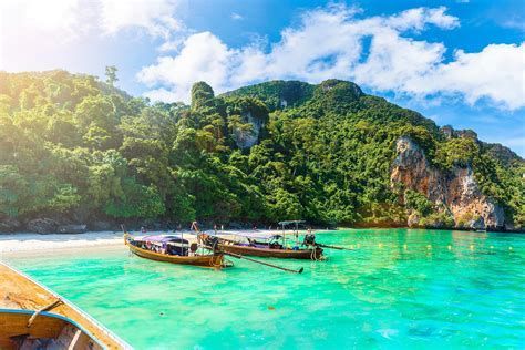 Two long-tail boats on turquoise water by a lush tropical island and blue sky
